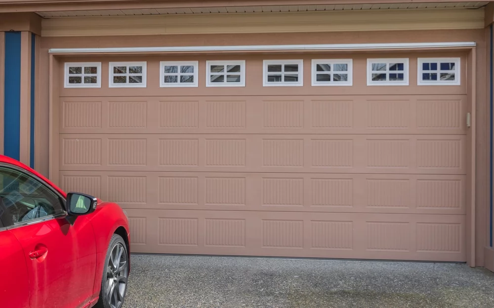 A closeup on a garage door, with a red car in the driveway.