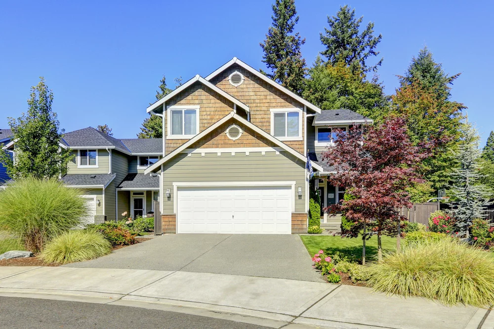 The garage door of a beautiful new home, surrounded by trees.