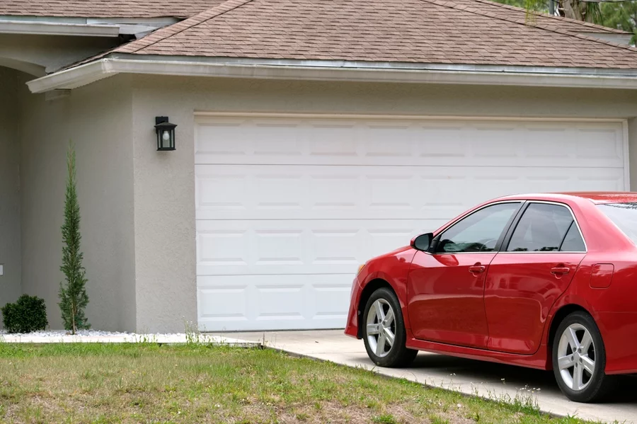 A garage with a red sedan in the driveway.